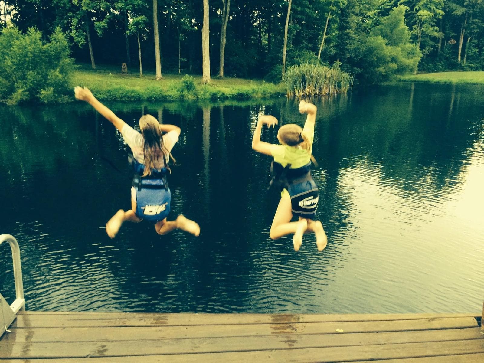 Two children jumping from a dock into a wooded pond