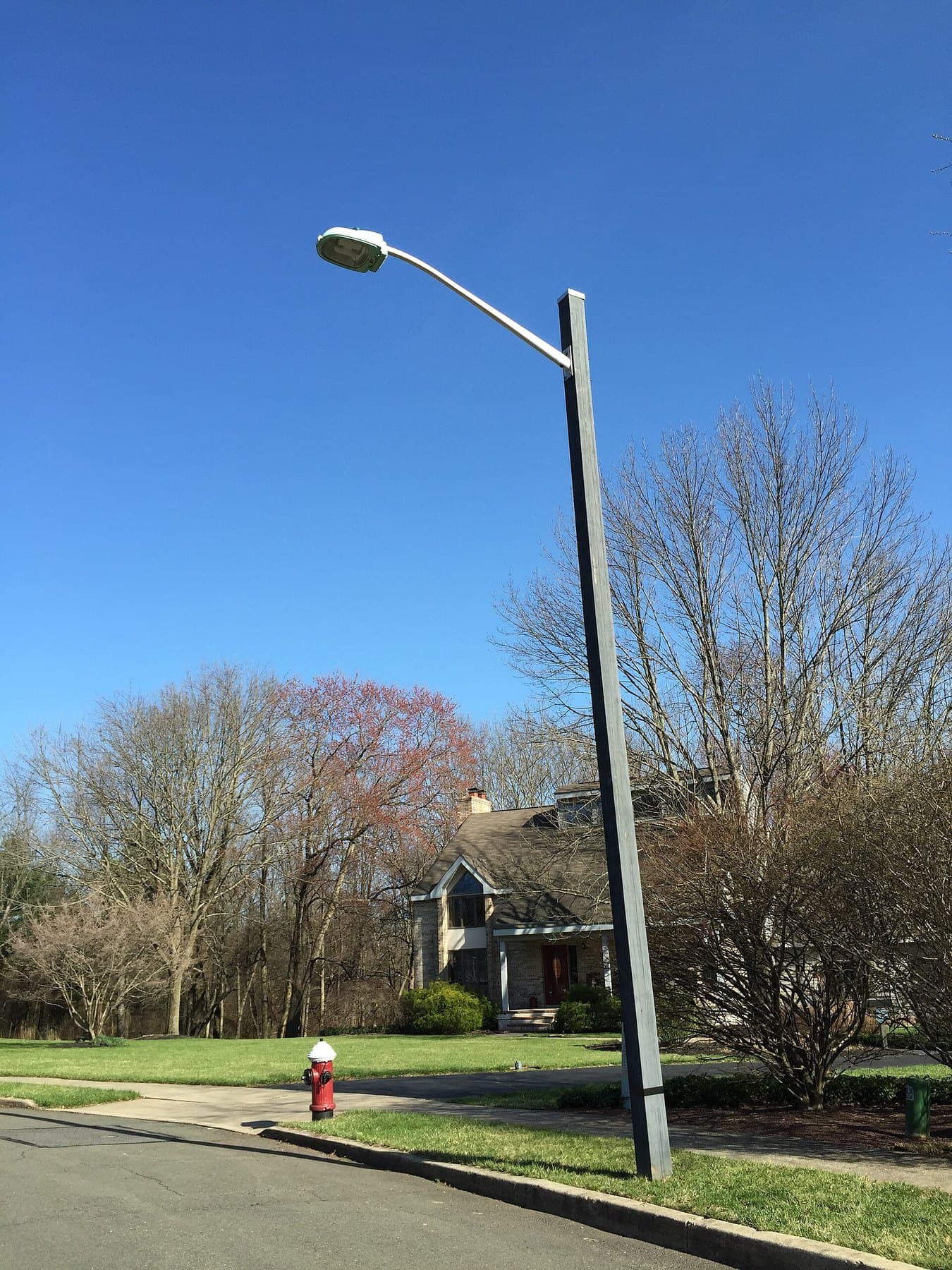 A pole-mounted street light beside a sidewalk and lawn in front of a house